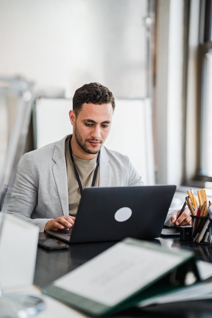 Focused man working on a laptop in a modern office setting, emphasizing productivity and technology.
