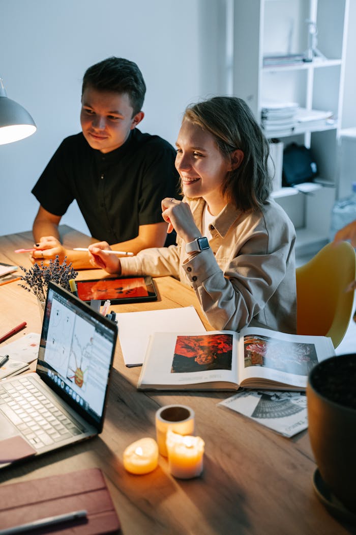 Two young professionals working together in a cozy, modern workspace with laptops and books.