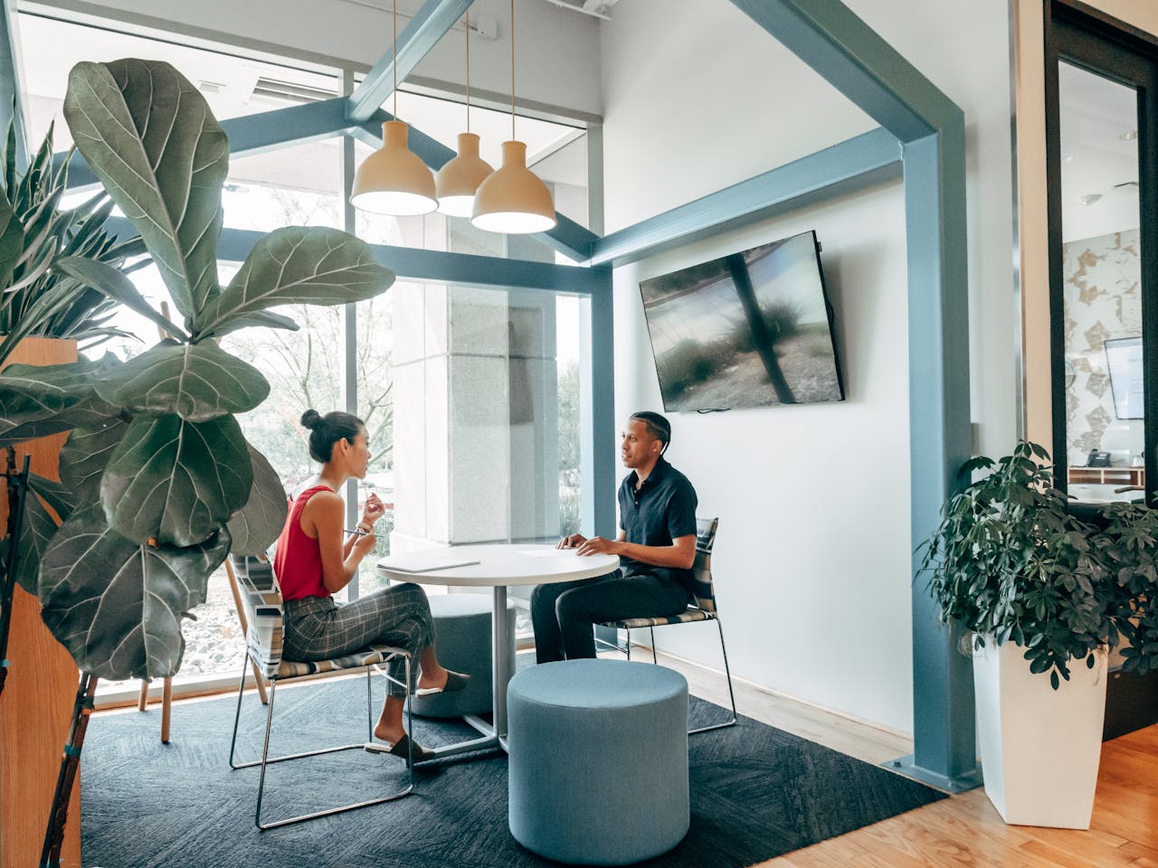 Two colleagues in a modern office space having a discussion with indoor plants and stylish decor.